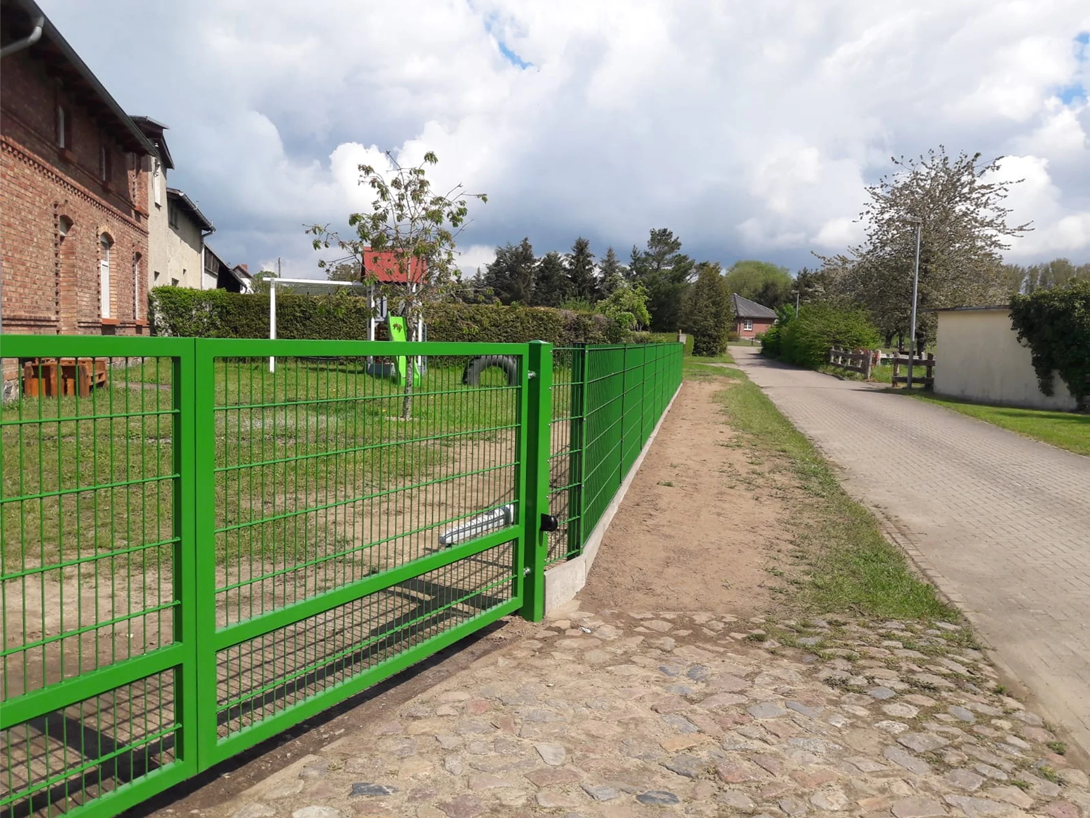 Grünes Stahltor mit Doppelflügel und Zaun