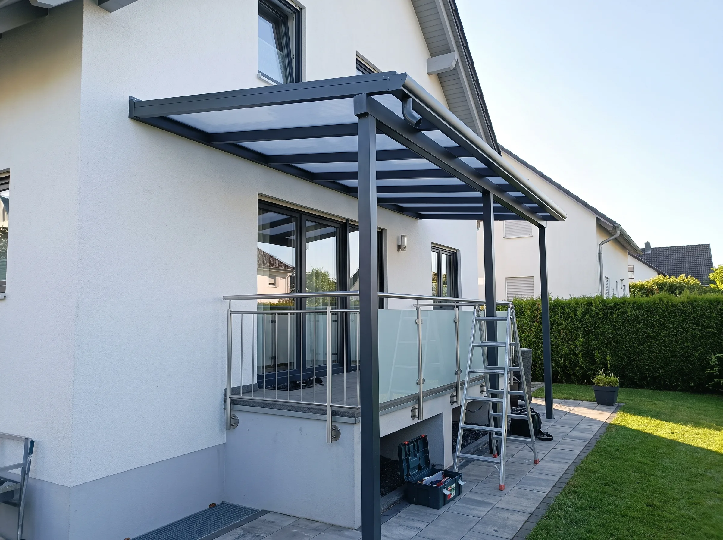 Überdachung eines Balkons mit Glasgeländer und Treppenleiter im Garten
