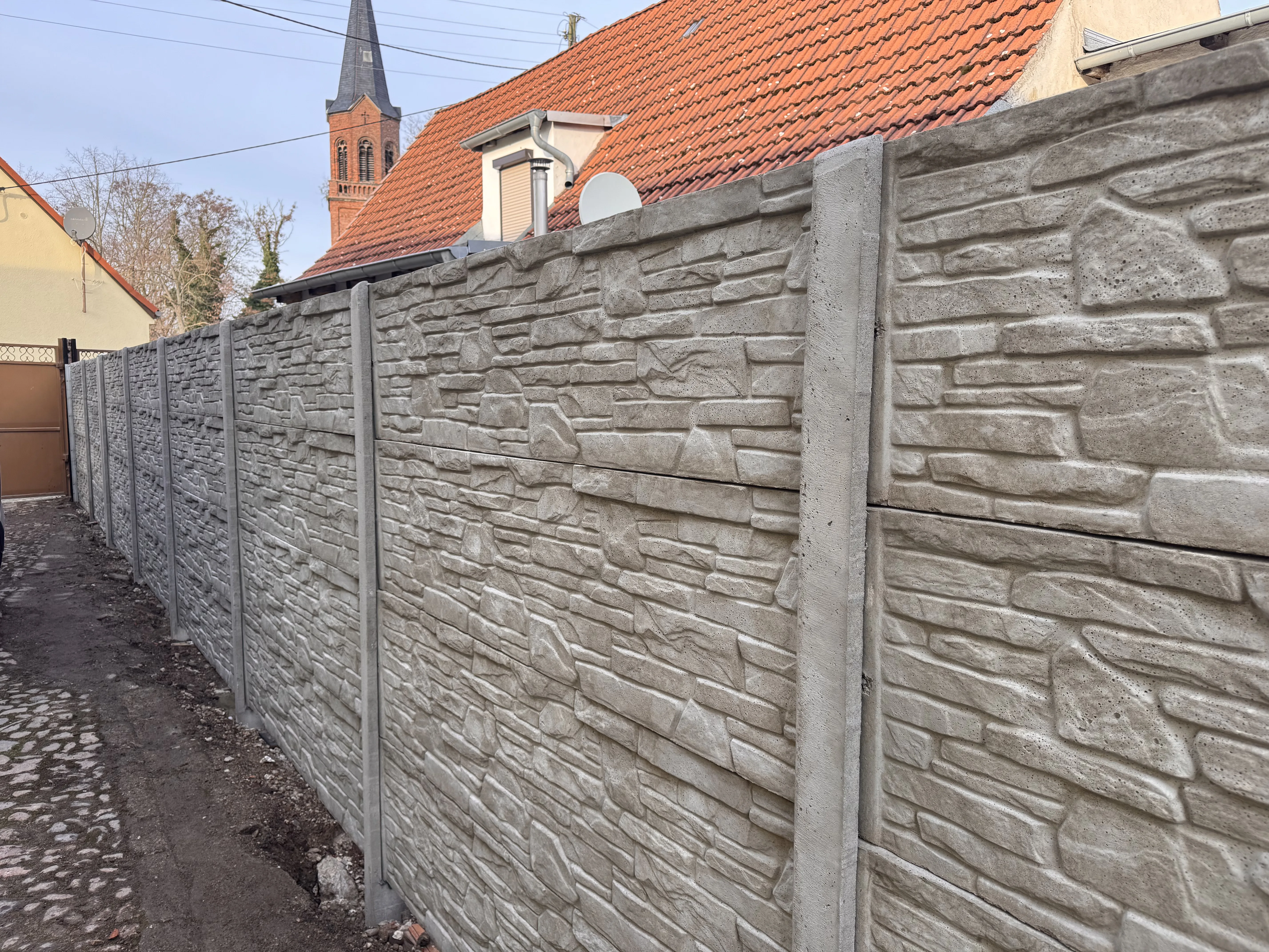 Moderner Betonzaun mit Steinoptik entlang einer Straße