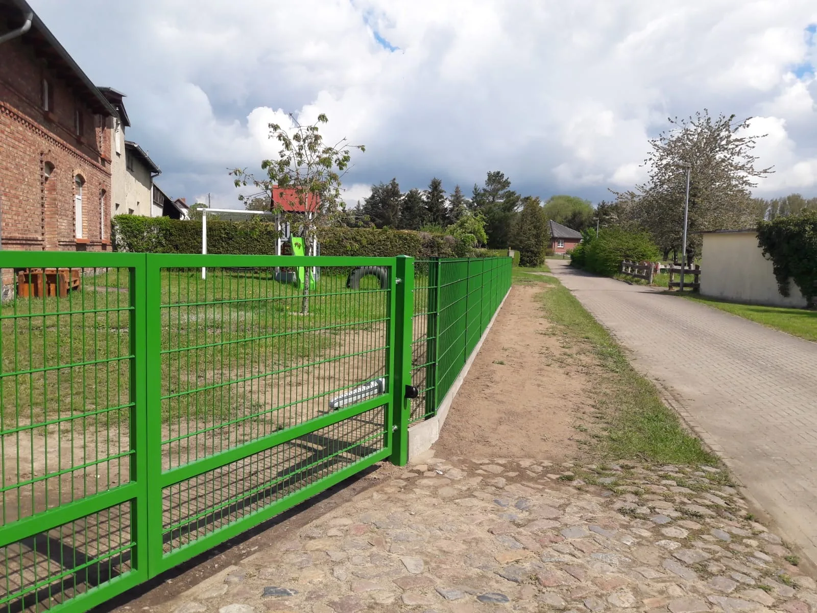 Moderner Doppelstabmattenzaun in leuchtendem Grün, umgeben von einer gepflegten Gartenlandschaft