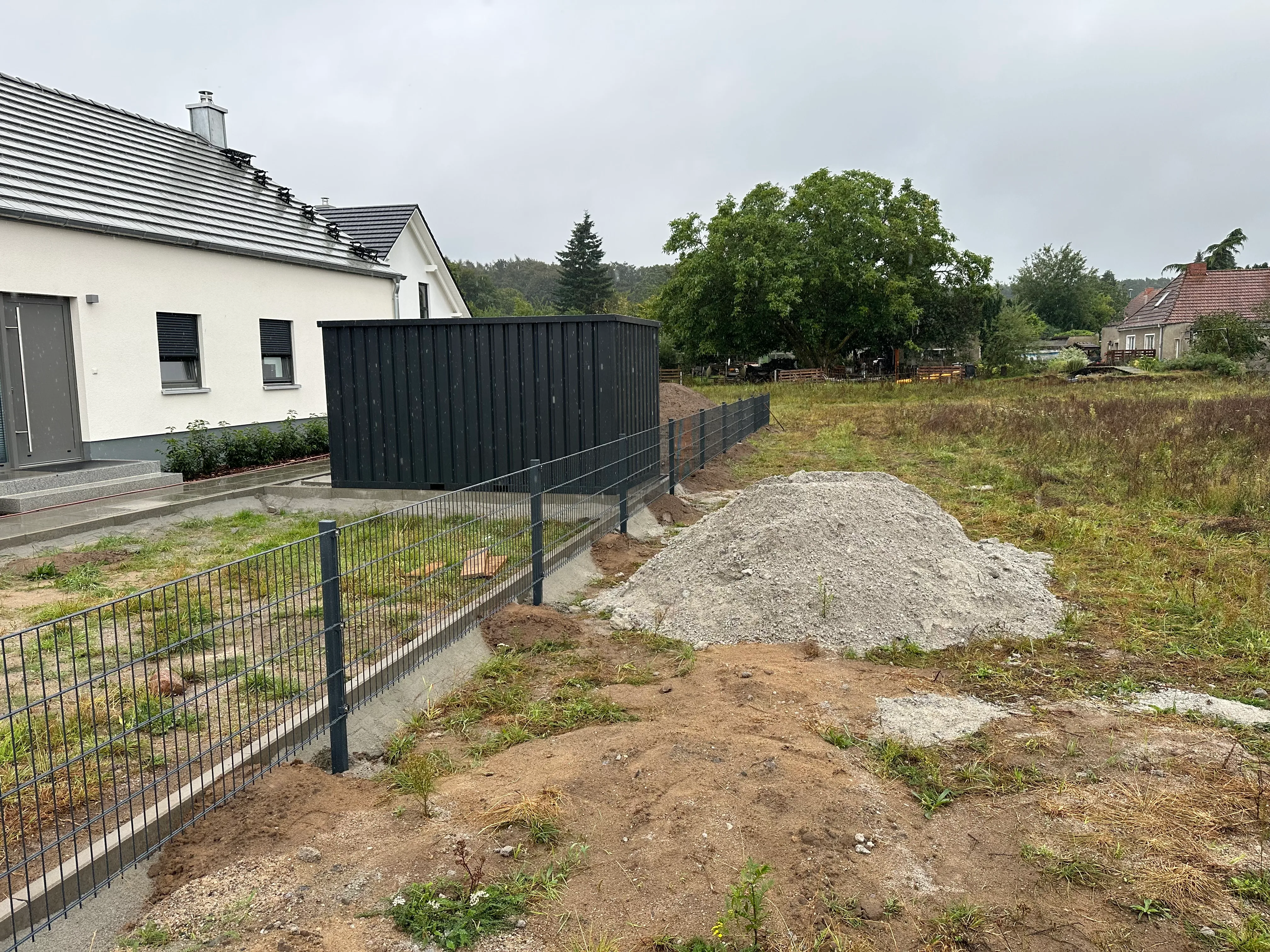 Sichtschutzzaun aus Doppelstabmatten umgibt ein Grundstück mit unberührtem Rasen und einem Holzschuppen