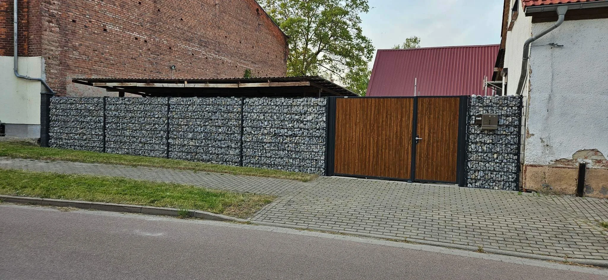 Moderner Gabionenzaun mit Holztor und Sichtschutz in einer urbanen Umgebung