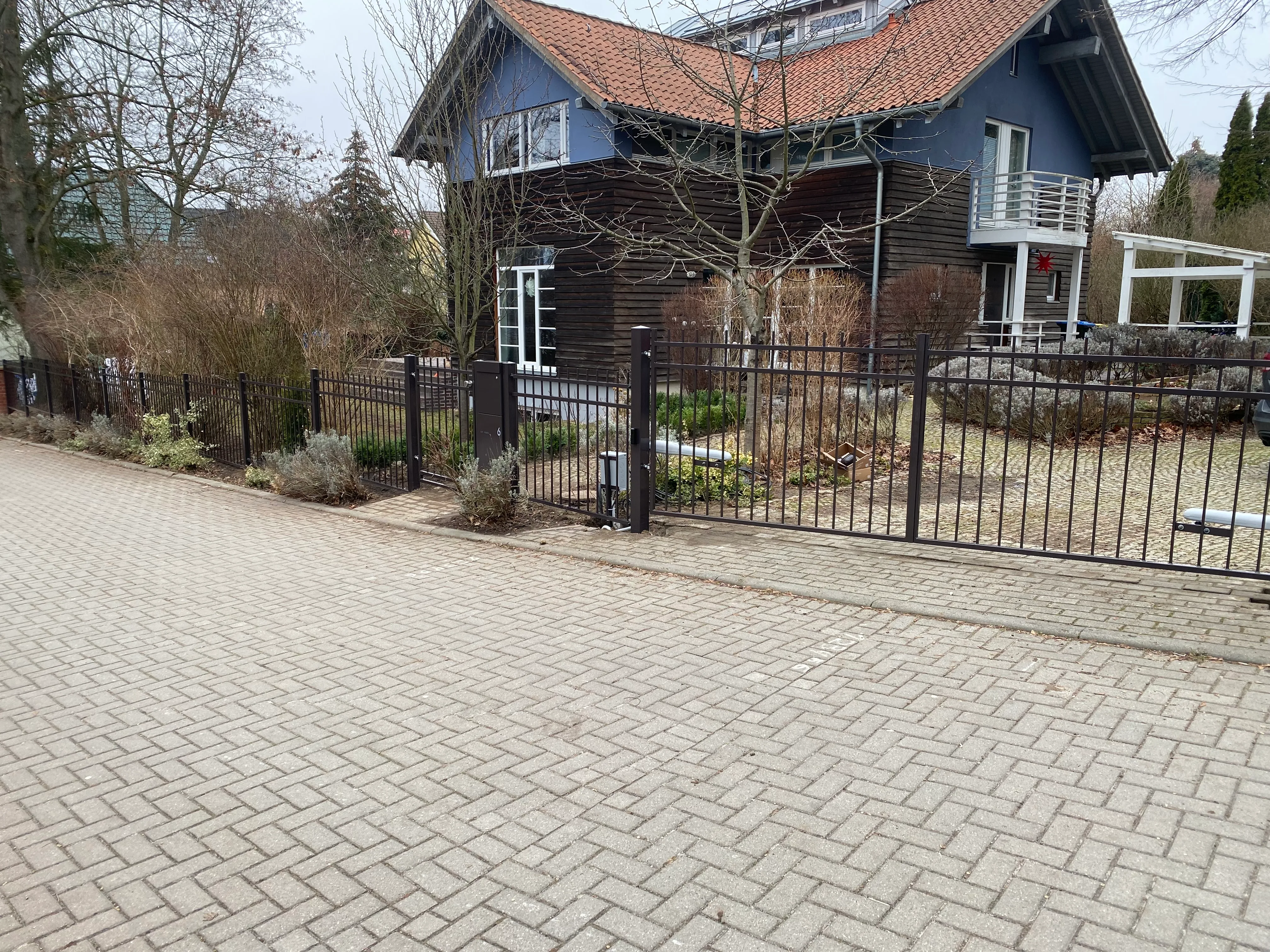 Moderner Zaun aus Metall vor einem Garten und einem Haus