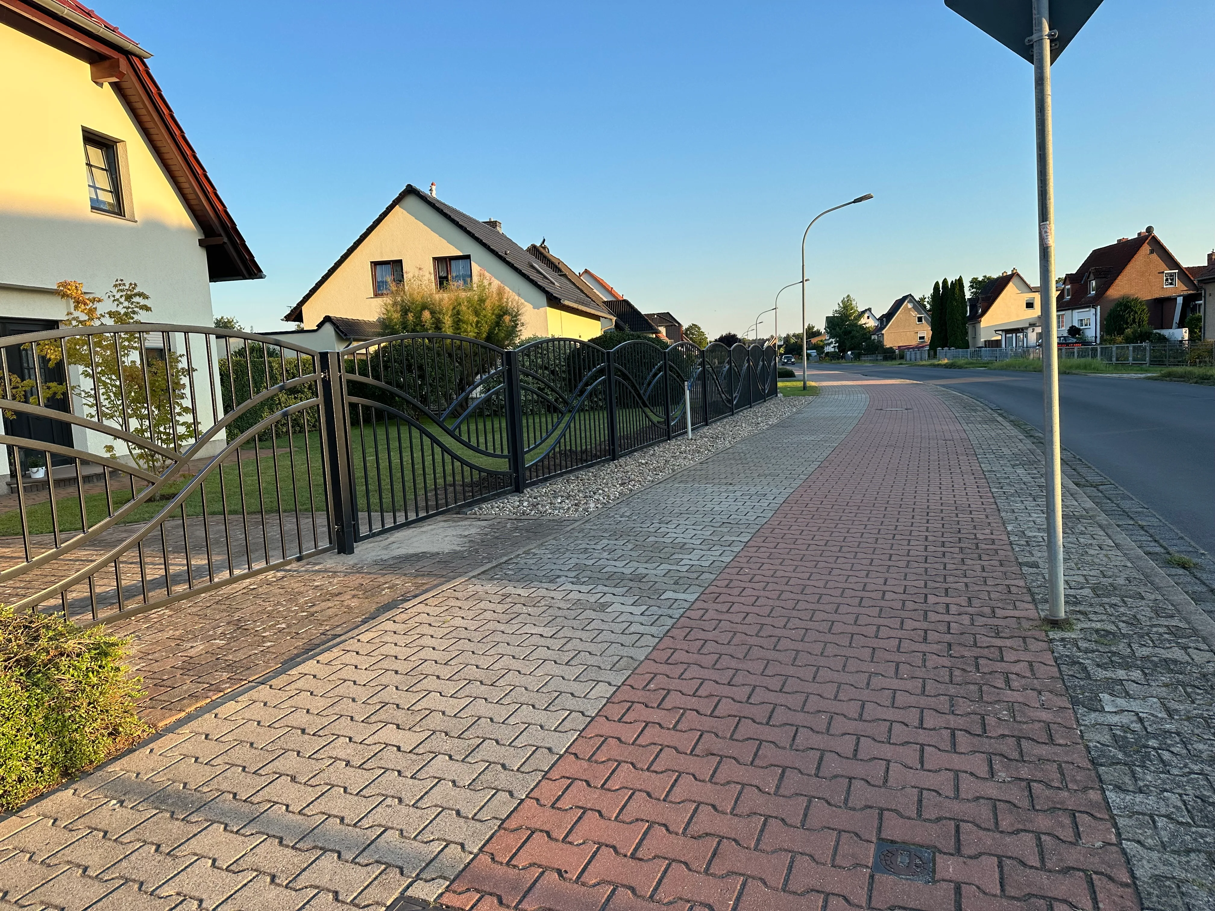 Moderner Zaun rechts mit Wellenmuster in Wohngegend, umgeben von Wiese und Asphaltweg