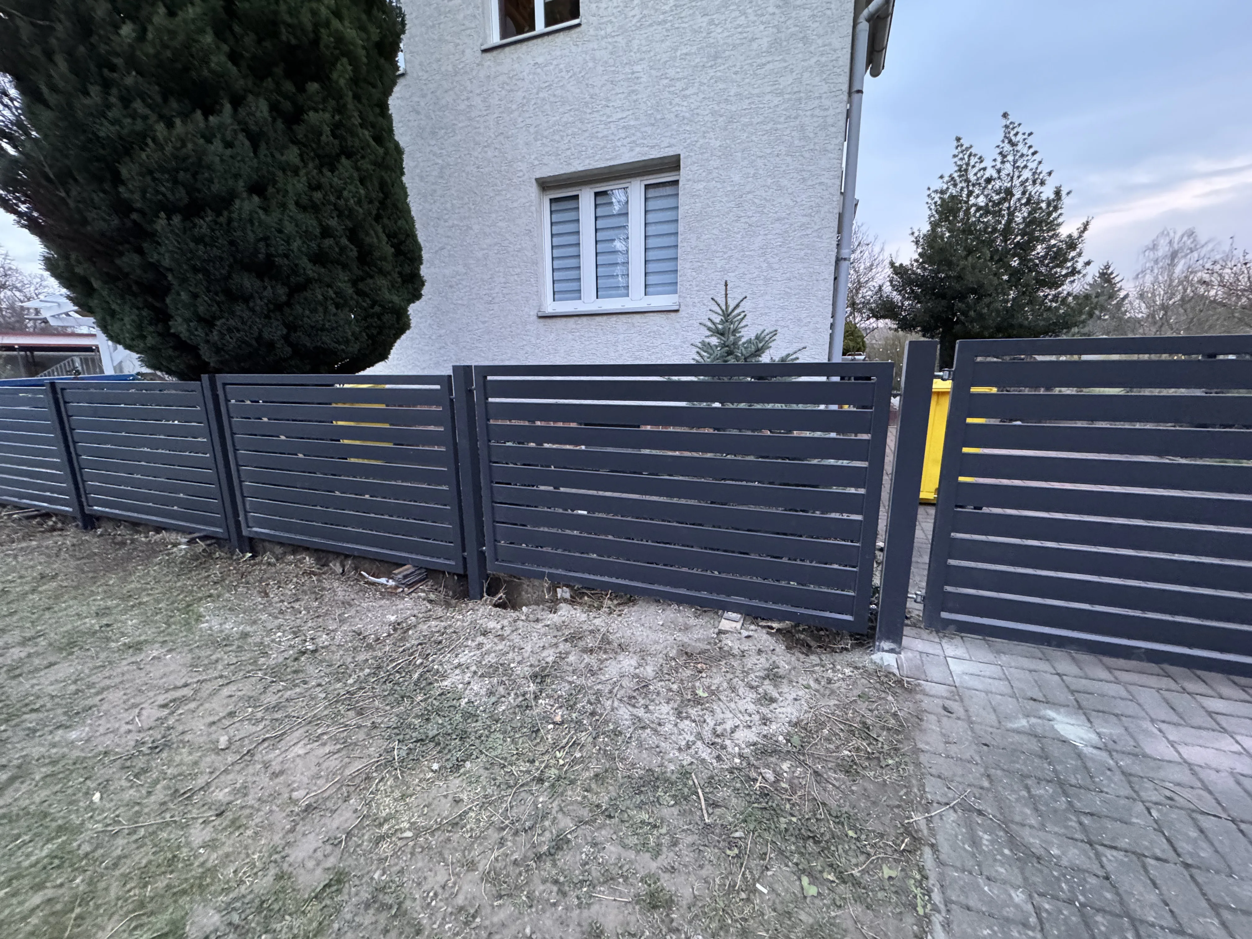 Moderner Sichtschutzzaun in dunkler Farbe, umgeben von Gras und Bäumen, an einem Wohnhaus