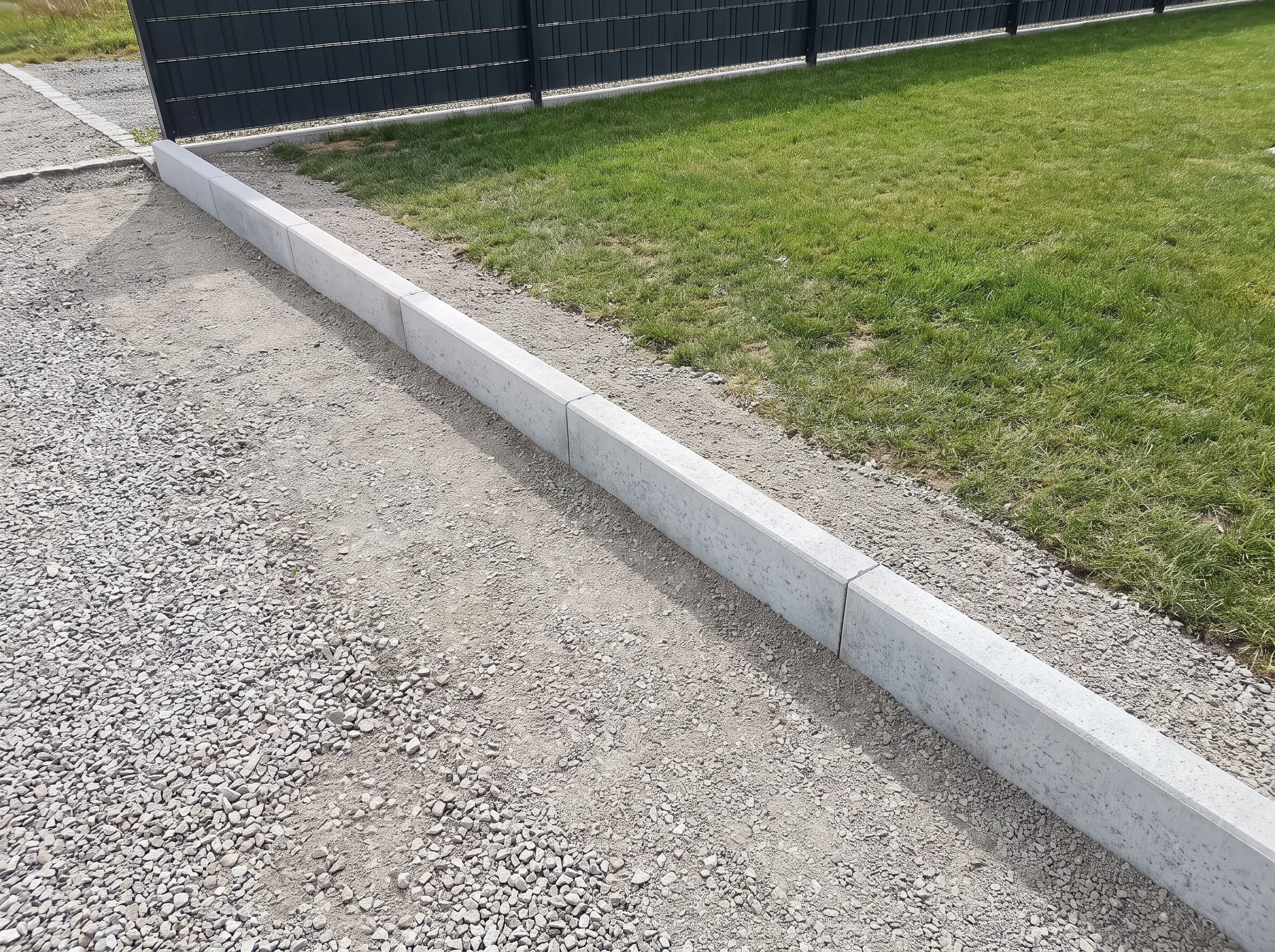 Betonrandsteine, die an einem Zaun verlegt sind, um den Gartenbereich abzugrenzen