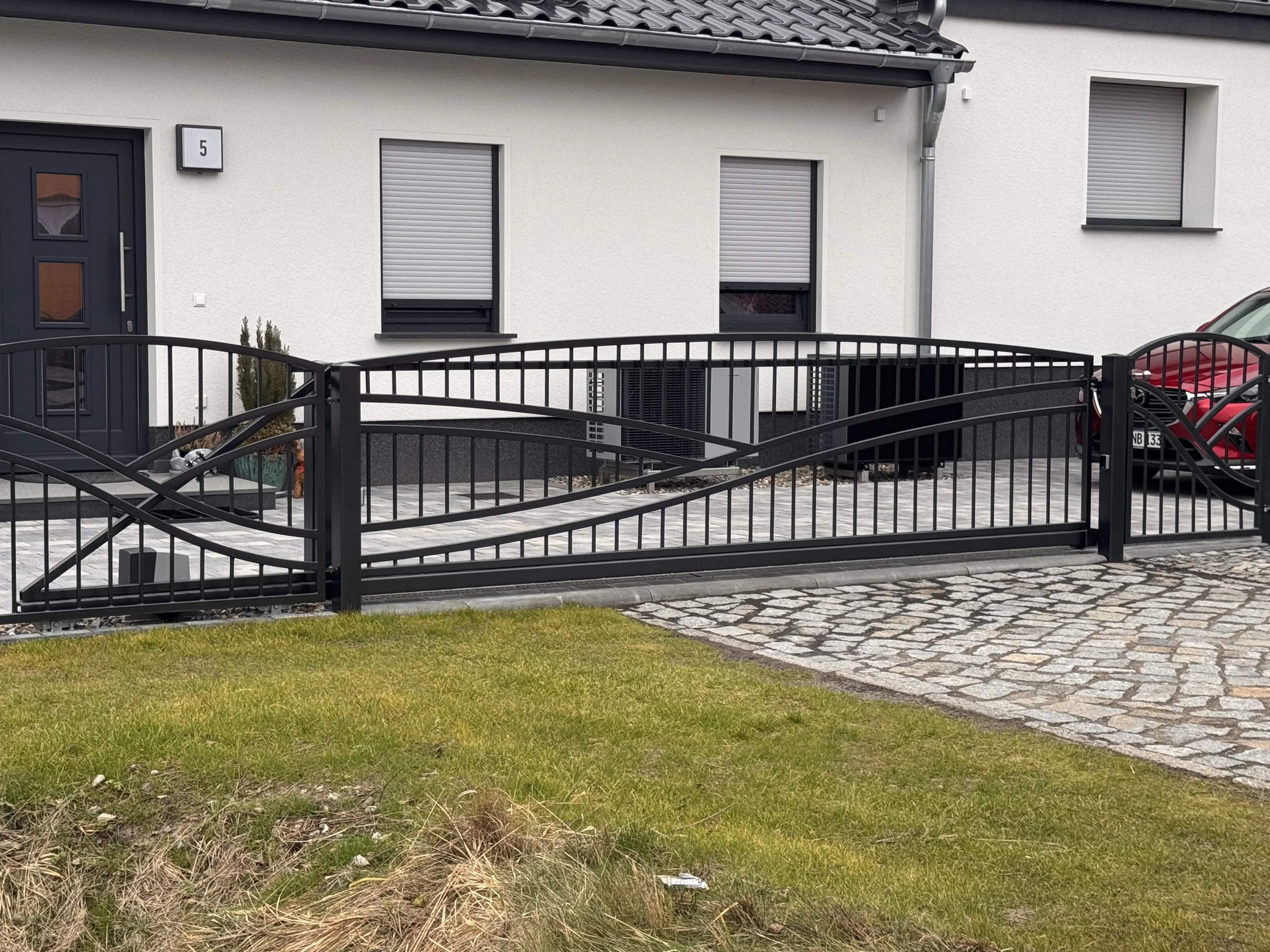 Modernes Gartentor mit geschwungenen Elementen vor einem modernen Wohnhaus
