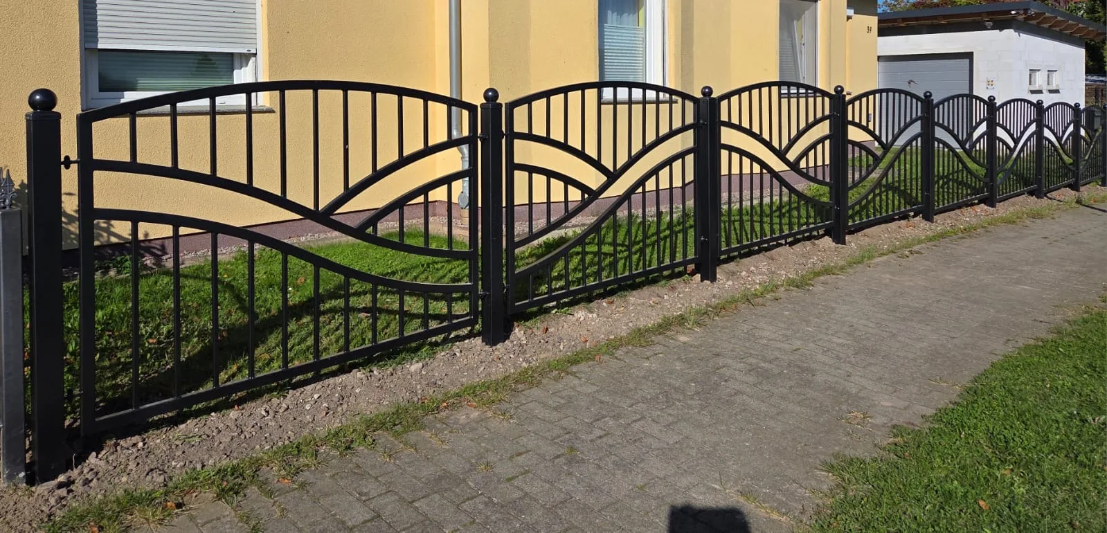 Moderner Zaun mit beeindruckendem Wellenmuster entlang des Gehwegs